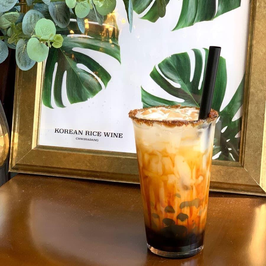 餐廳內的黑糖馬格利酒，背景是綠植裝飾，玻璃杯內巧妙層次展現黑糖和馬格利的融合。」